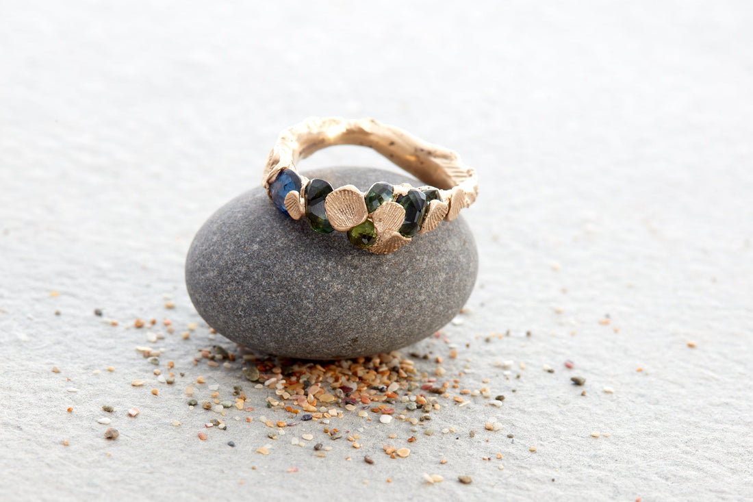 Sculptural one of a kind gold ring handcrafted in North Devon. The Sea Form Ring features shell imprints, grains of sand, and natural green-blue sapphires  a wearable fragment of the coastal landscape, lost wax carved and cast in ethical recycled gold.