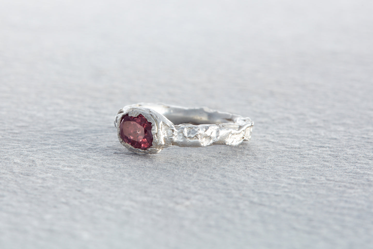 Organic sculptural silver ring with raspberry sapphire set in uneven rock like textured surface inspired by natural forms