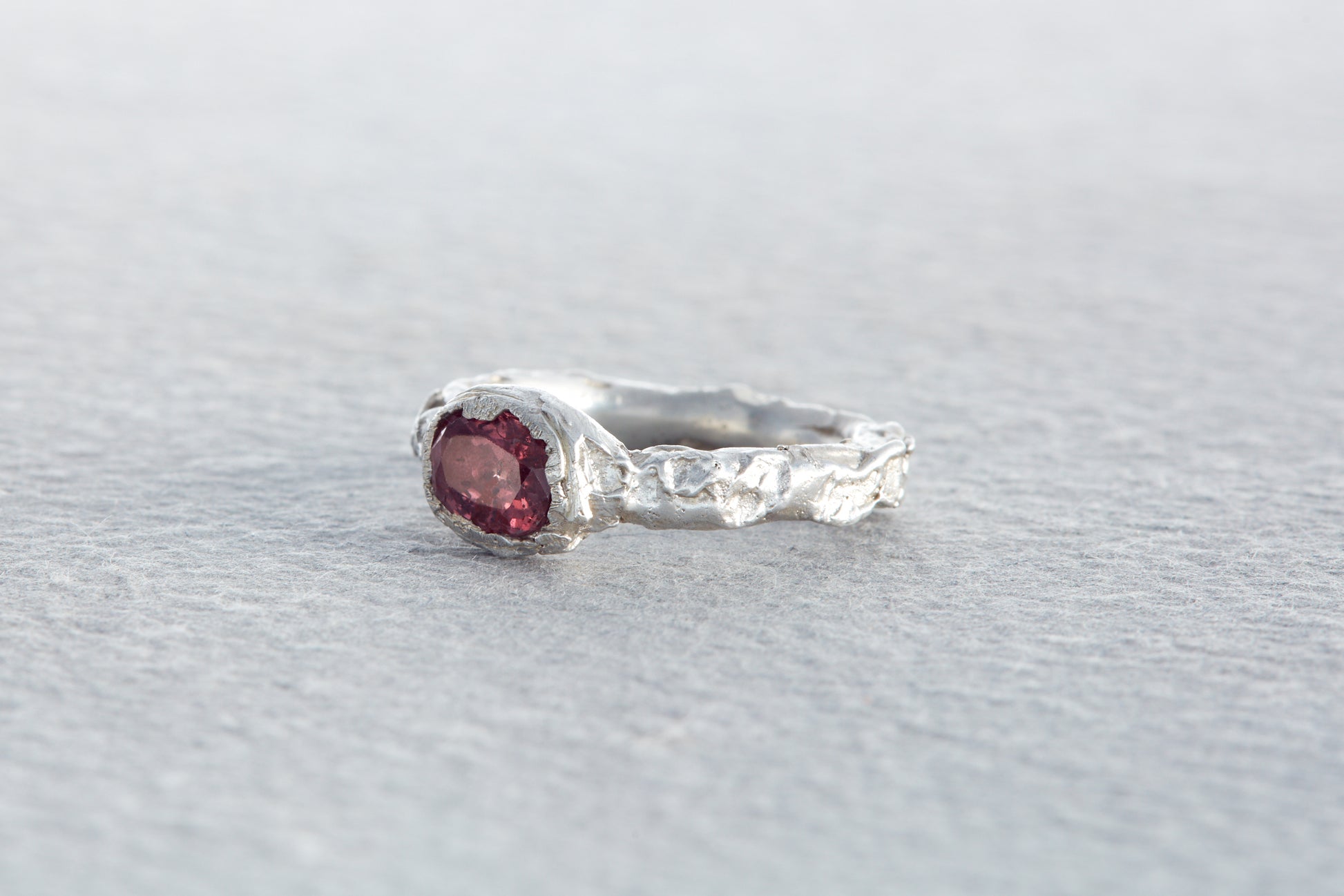Organic sculptural silver ring with raspberry sapphire set in uneven rock like textured surface inspired by natural forms