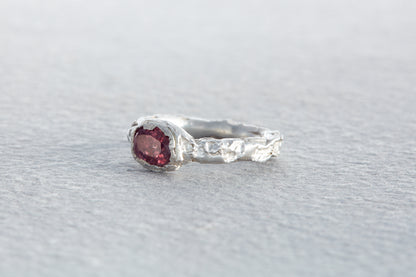 Organic sculptural silver ring with raspberry sapphire set in uneven rock like textured surface inspired by natural forms