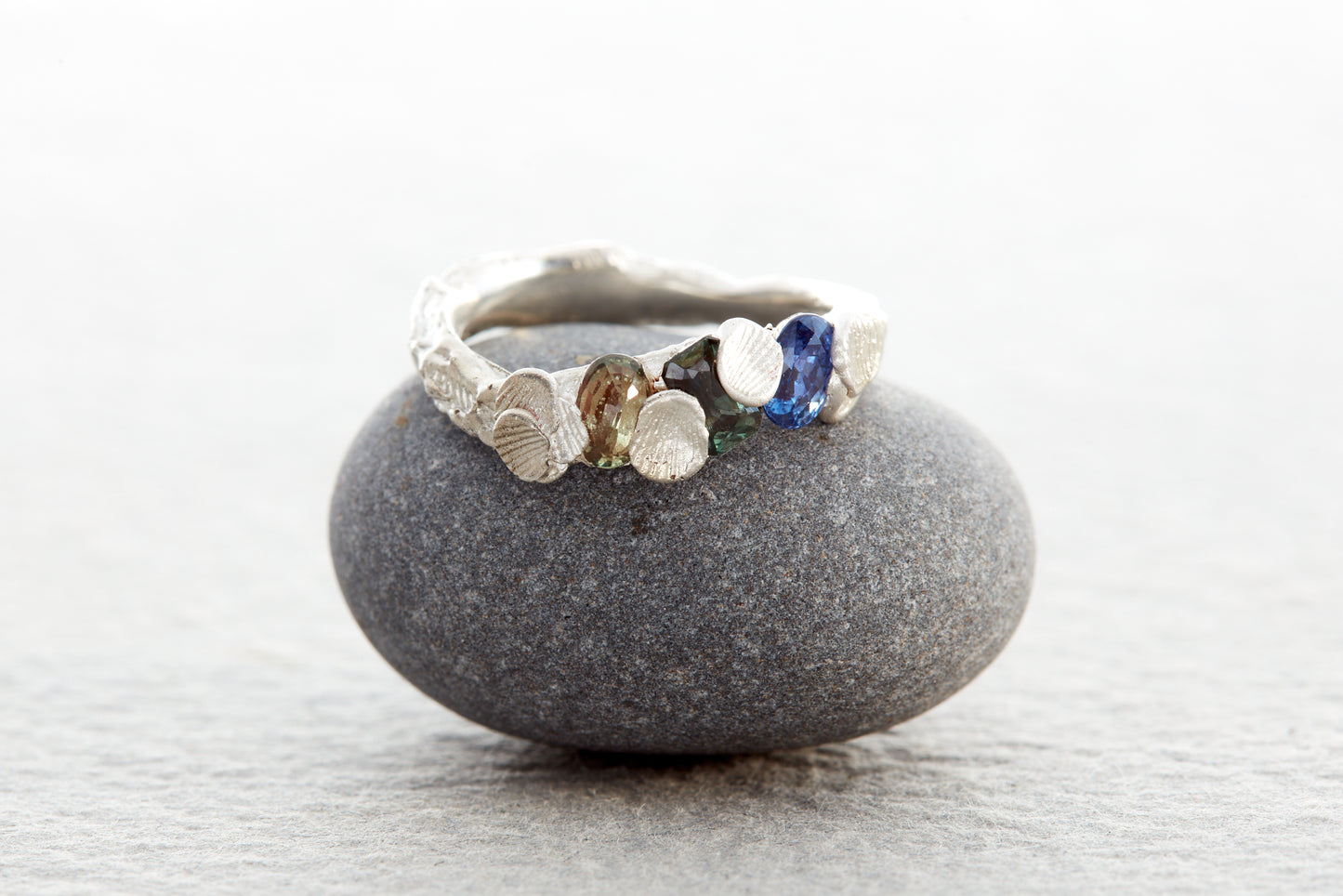 Sculptural silver Shellscape ring formed with organic textures inspired by the Devon coastline, set with ocean-toned sapphires in blue, teal and green.