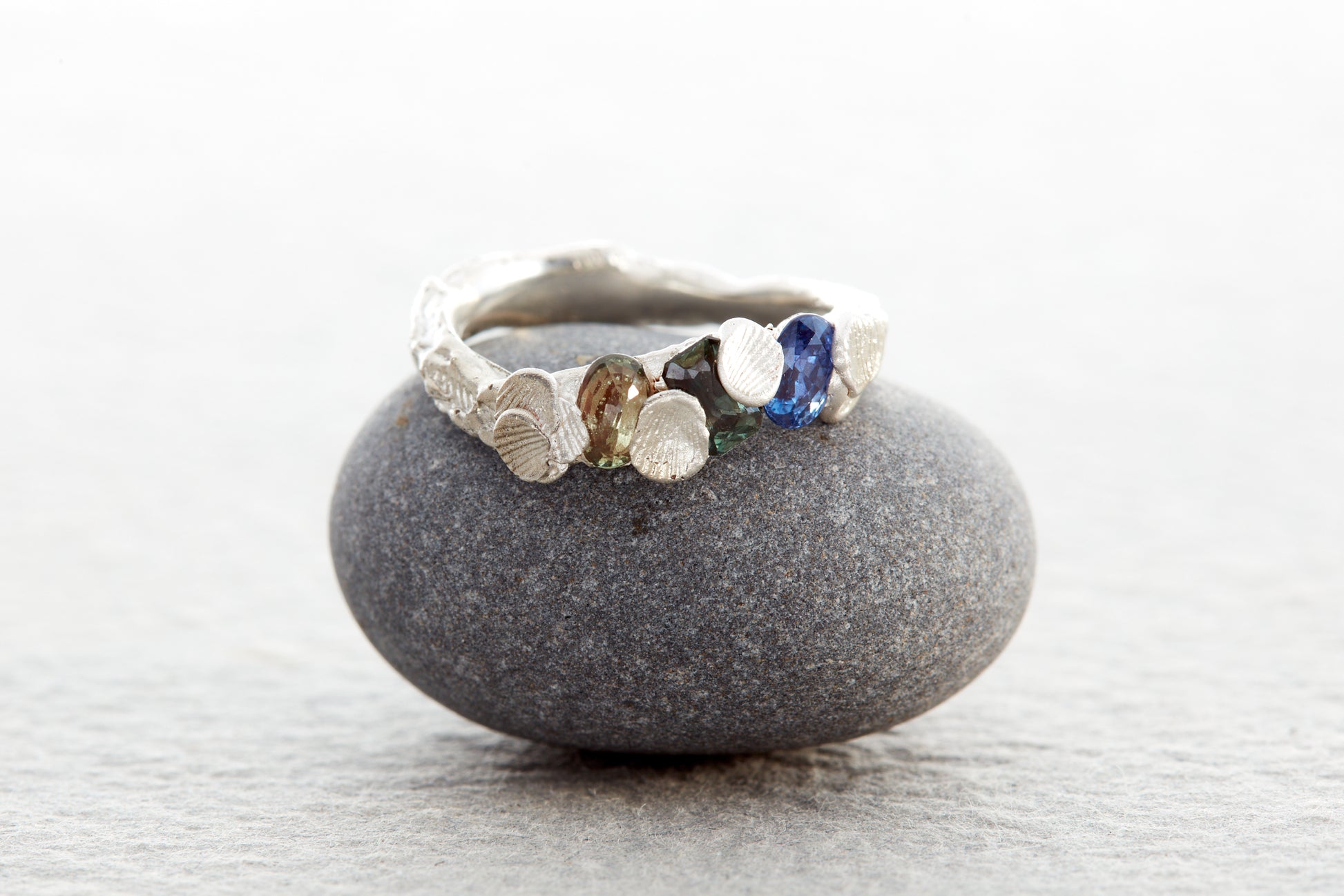 Sculptural silver Shellscape ring formed with organic textures inspired by the Devon coastline, set with ocean-toned sapphires in blue, teal and green.