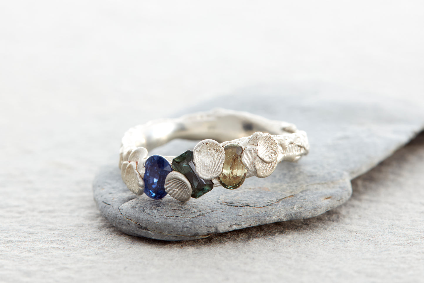 Handcrafted sculptural silver Shellscape ring with organic textured surface inspired by ocean shoreline and natural coastal forms, set with blue, teal and soft green sapphires.