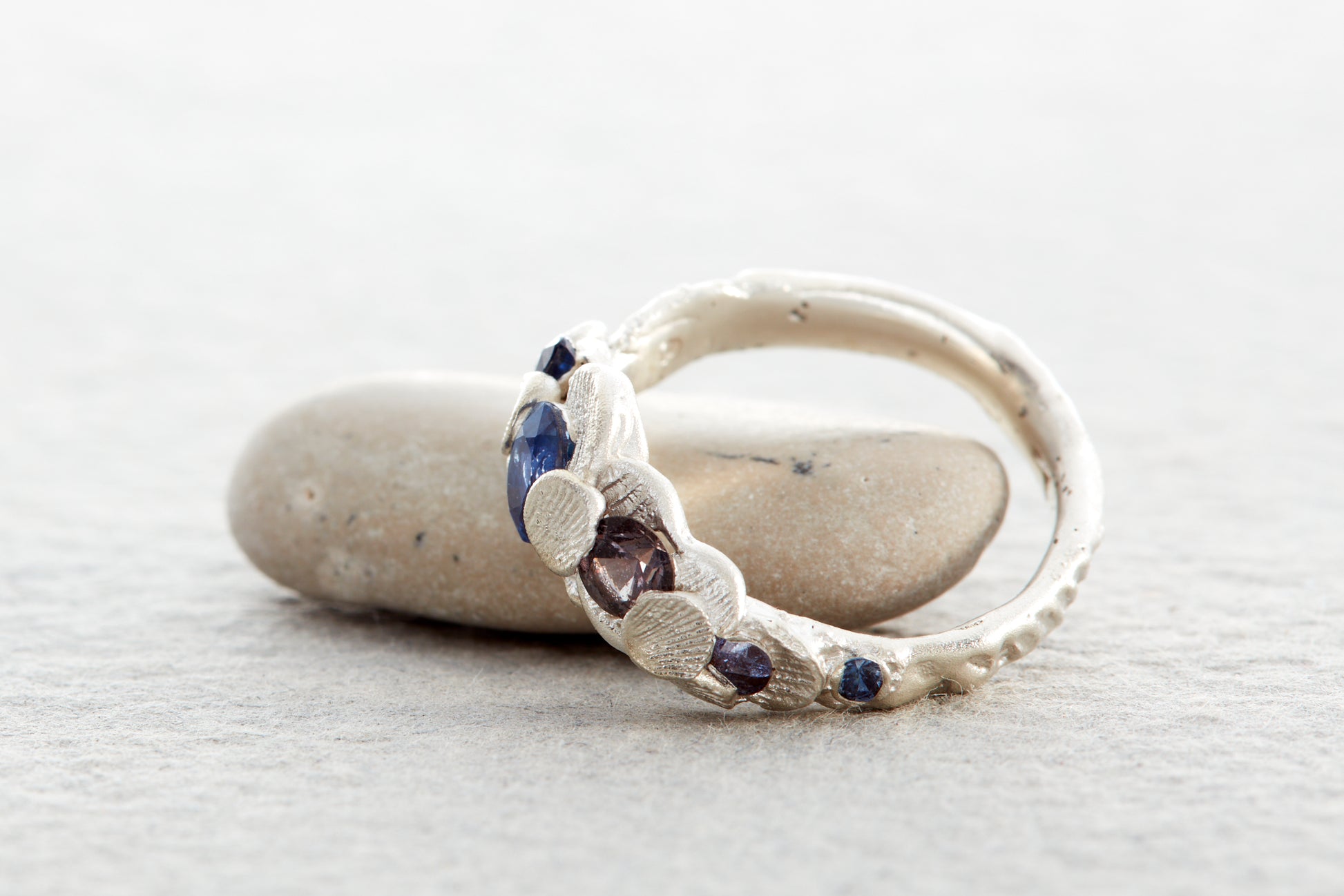Handmade sculptural silver ring with blue sapphires and seaweed toned gemstone reflecting coastal light of North Devon UK