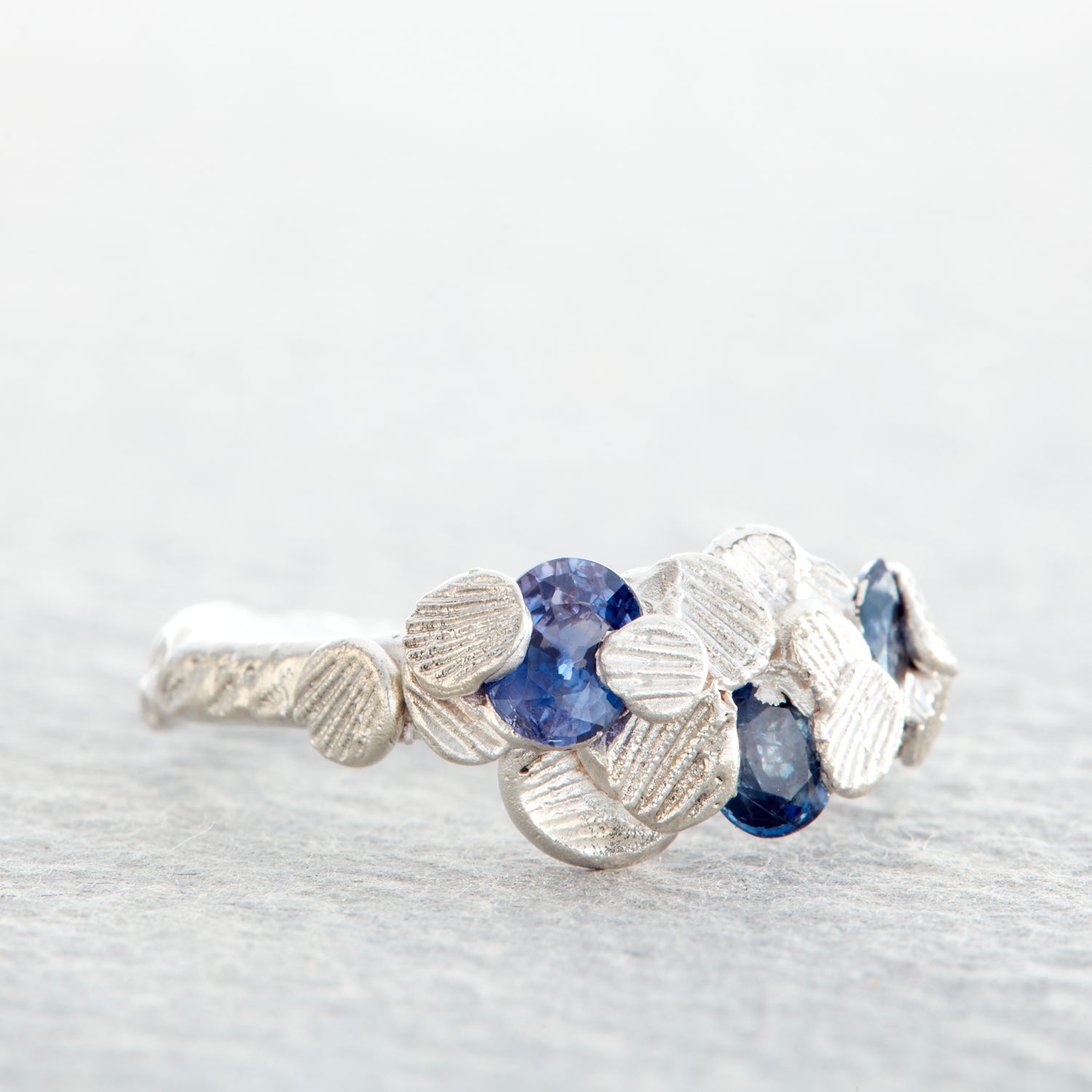 Custom organic anniversary ring in silver featuring a cluster of Sri Lankan blue sapphires nestled among hand cast sea shells